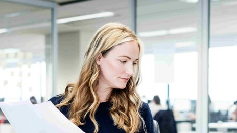 Professional reviewing documents and working on a laptop in a modern office.