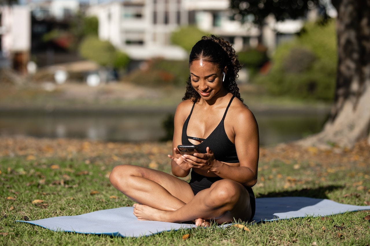 Smiling and using texting abbreviations in English while on yoga mat in park.