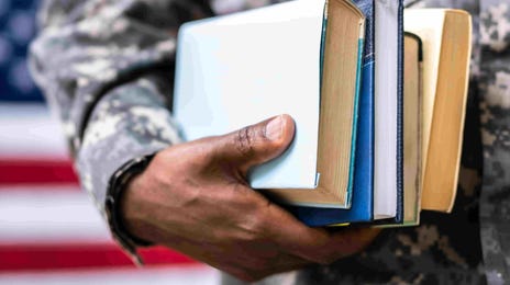 A U.S. service member holding books, standing in front of the American flag, symbolizing education and duty.