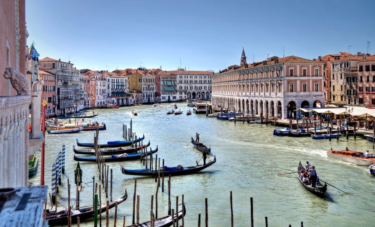 Grand canal in Venice Italy featuring gondalas, people learning Italian for free with locals, and buildings.