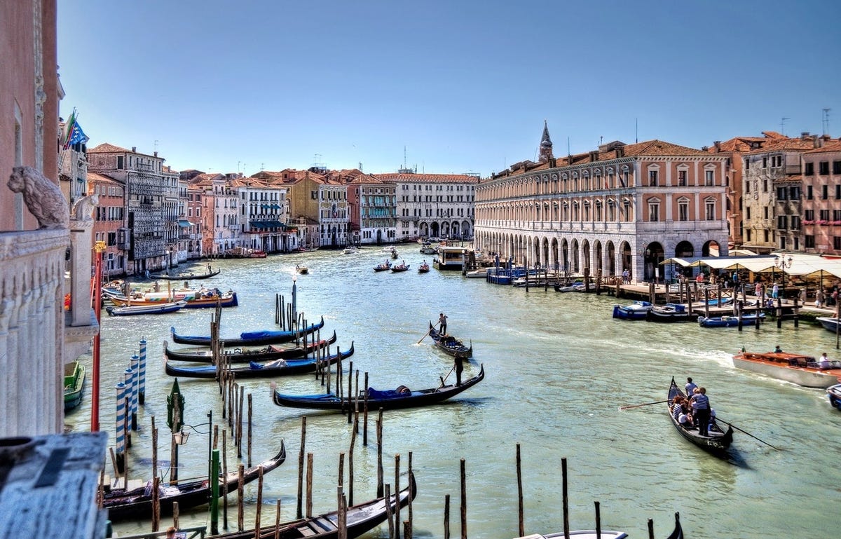 Grand canal in Venice Italy featuring gondalas, people learning Italian for free with locals, and buildings.