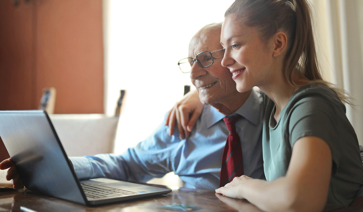 Grandfather sits with his granddaughter to have an online chat with other family members in German.