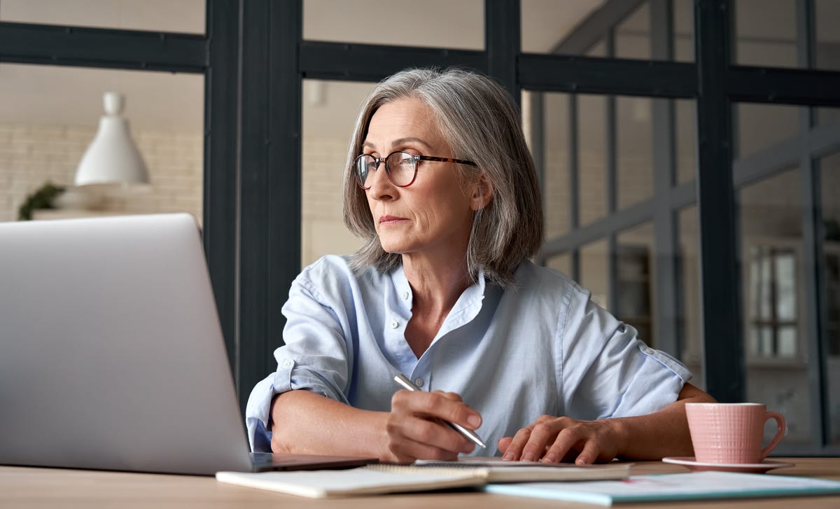 A senior woman taking notes and studying on her laptop, representing the opportunity to learn Marathi online in a modern, comfortable setting.
