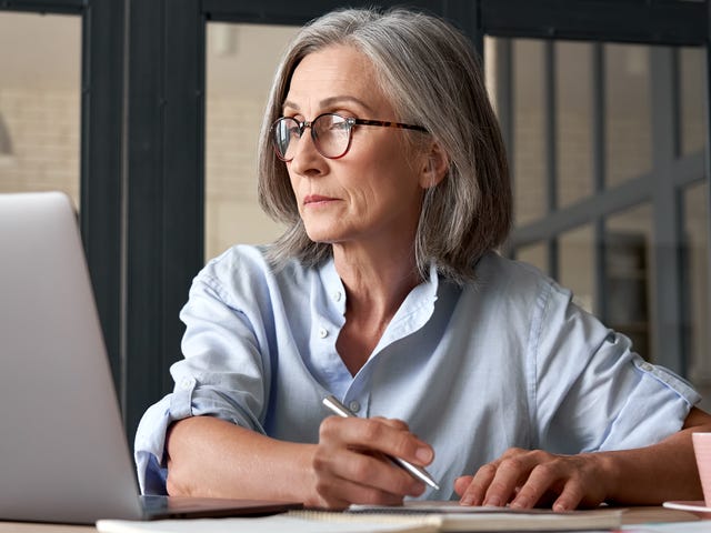 A senior woman taking notes and studying on her laptop, representing the opportunity to learn Marathi online in a modern, comfortable setting.