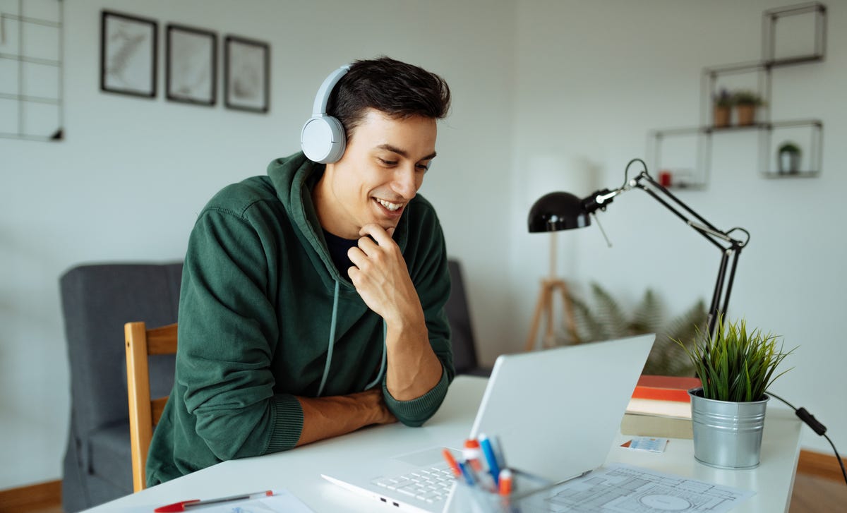 A young man wearing headphones smiles while studying on his laptop, representing an engaging way to learn Bulgarian online from home.