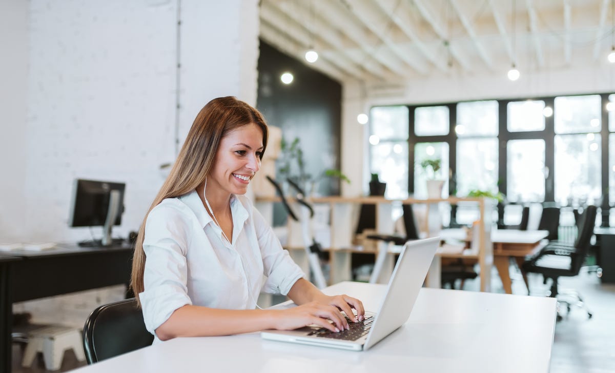 Smiling young woman with a laptop at a modern workspace, exploring opportunities in a French teaching career.