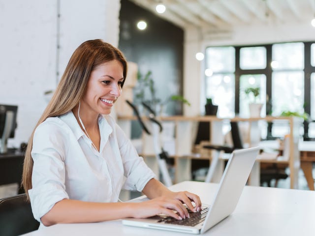 Smiling young woman with a laptop at a modern workspace, exploring opportunities in a French teaching career.