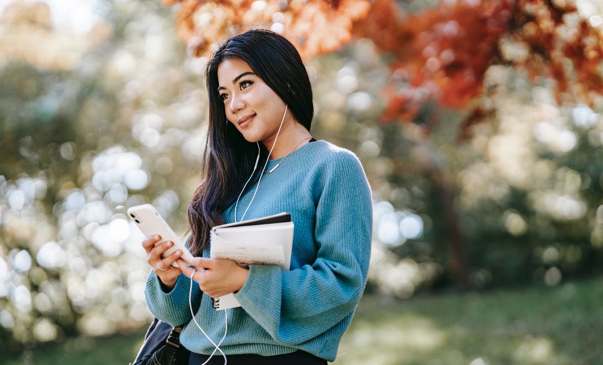 Young woman in a park with a notepad and smartphone, exploring opportunities in a Dutch teaching career.
