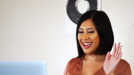 A woman smiling and waving at her laptop during an online class, representing a friendly and engaging way to learn Cantonese online.