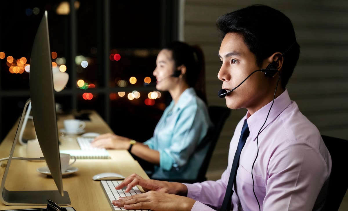 A man in a call center working at night with a headset on, representing remote learning opportunities to learn Malaysian online.