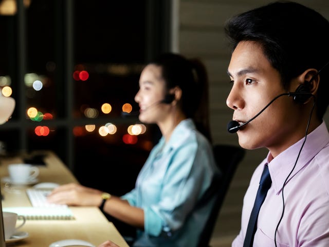 A man in a call center working at night with a headset on, representing remote learning opportunities to learn Malaysian online.