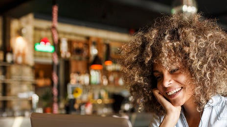 Smiling woman attending online Spanish classes for adults from a cozy café using her laptop