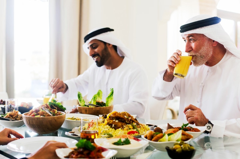 A group of men wearing traditional Middle Eastern attire sharing a meal together, representing cultural immersion and a community-driven way to learn Arabic online.