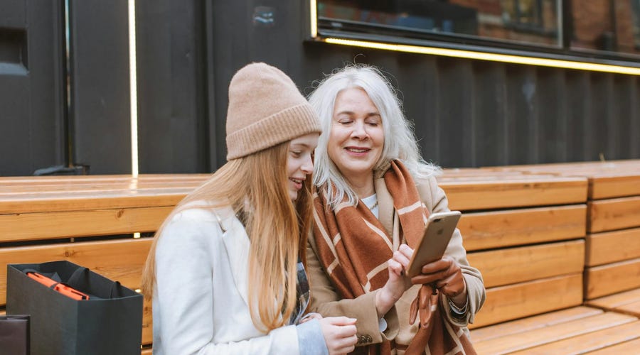 Two women sitting on a bench looking at a phone and learning about present perfect together