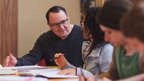A group of adult students taking Hungarian lessons together at a library table, discussing study materials.