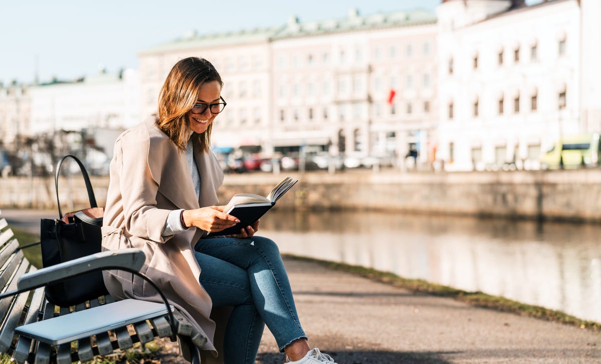 A woman sitting on a bench reading a book outdoors, representing a relaxed way to learn advanced German while enjoying a scenic environment.