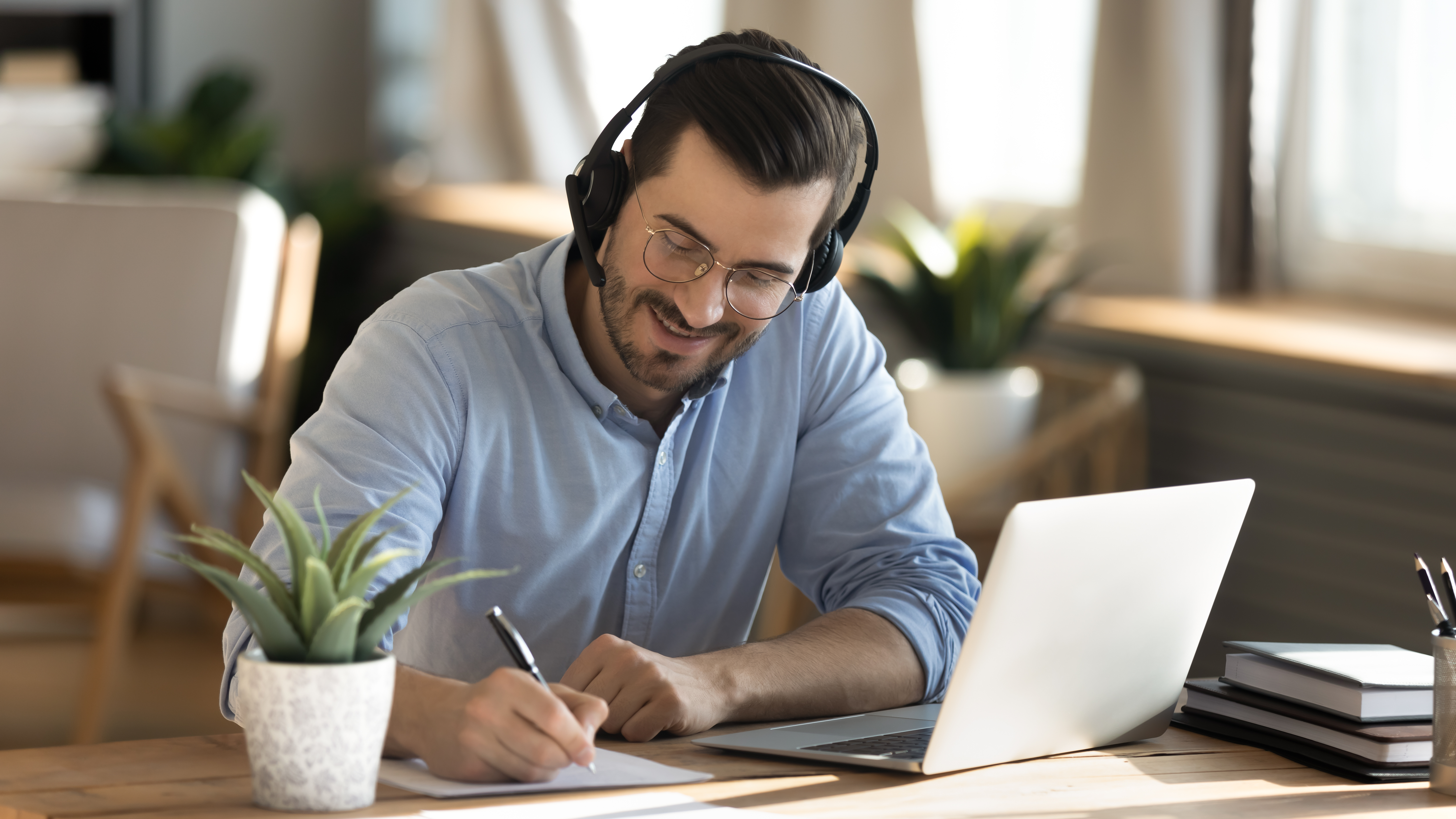 Man with headset writing notes while attending an online class to learn Romanian from home