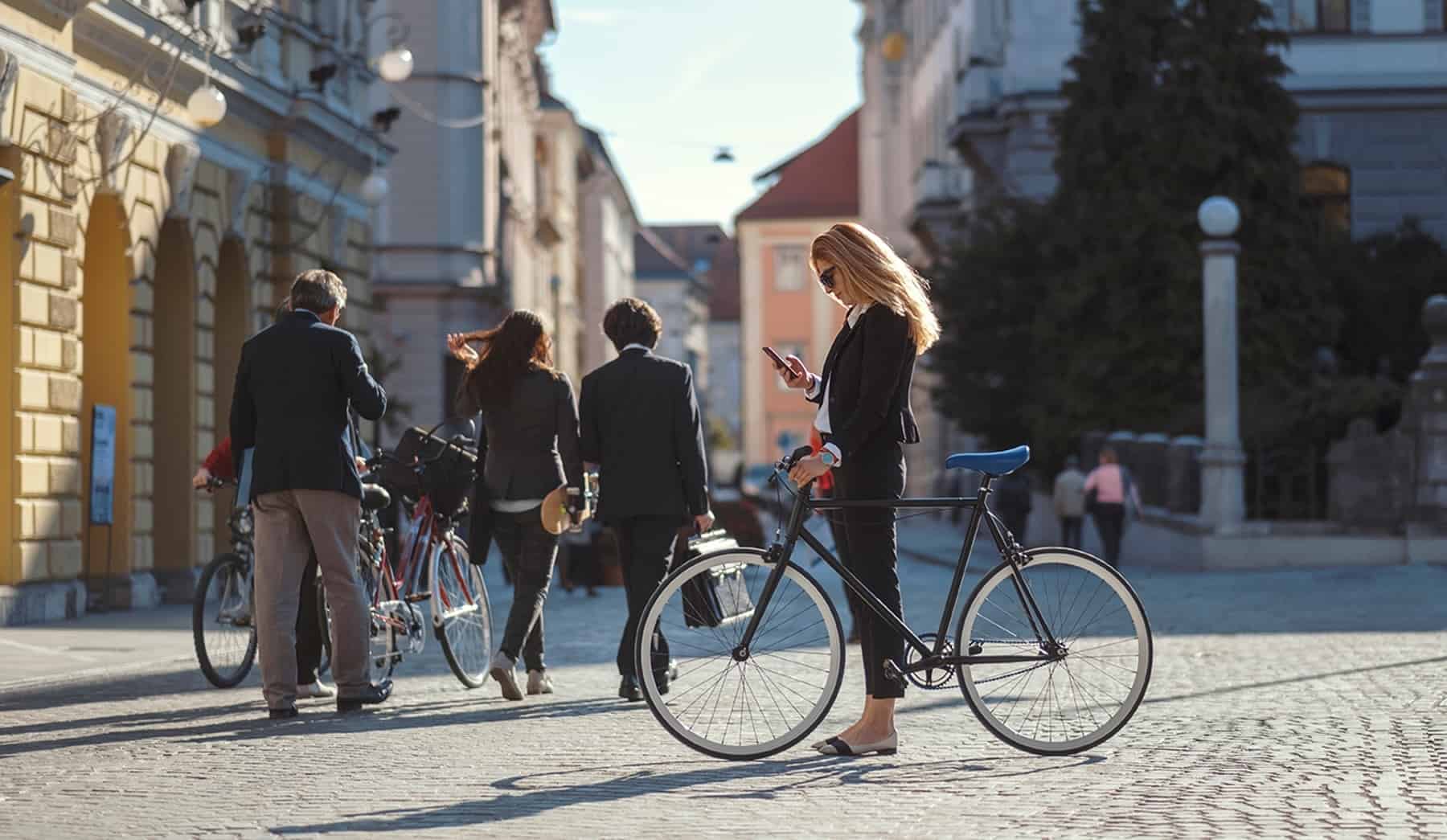 Confident woman checking her phone beside a bicycle in a European city, symbolizing the flexibility and lifestyle benefits of taking Italian courses online with Berlitz.

