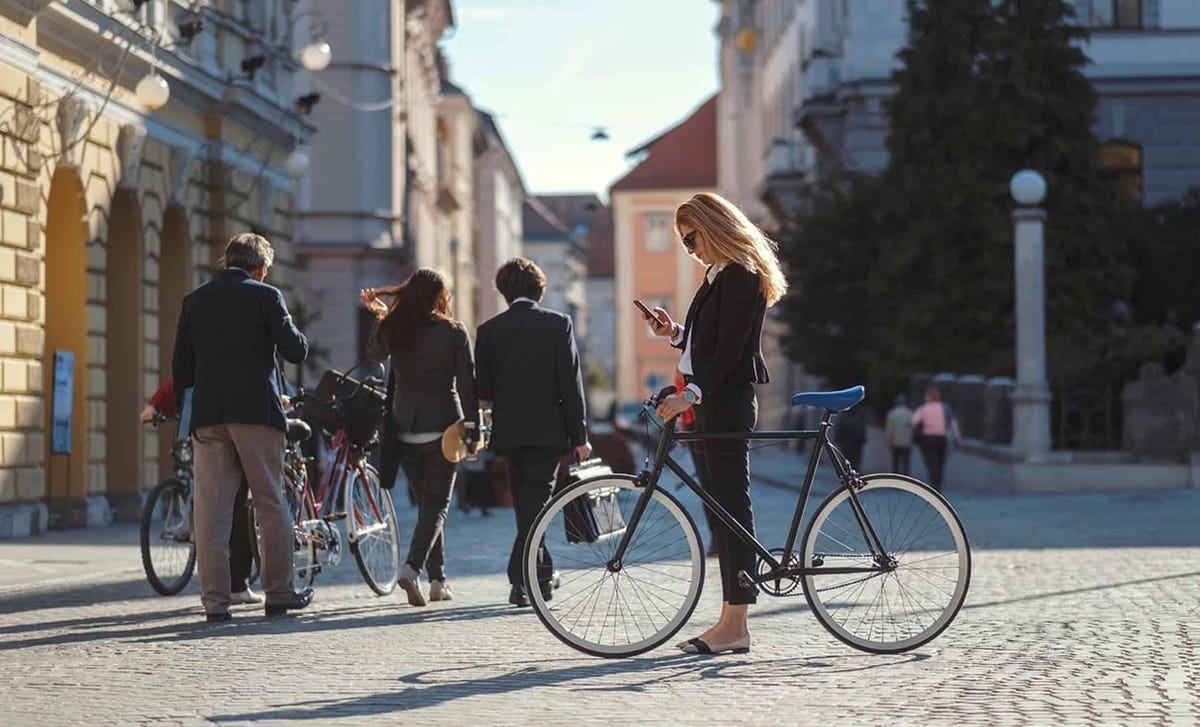 Confident woman checking her phone beside a bicycle in a European city, symbolizing the flexibility and lifestyle benefits of taking Italian courses online with Berlitz.