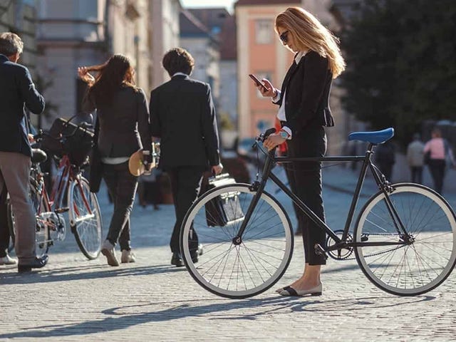 Confident woman checking her phone beside a bicycle in a European city, symbolizing the flexibility and lifestyle benefits of taking Italian courses online with Berlitz.