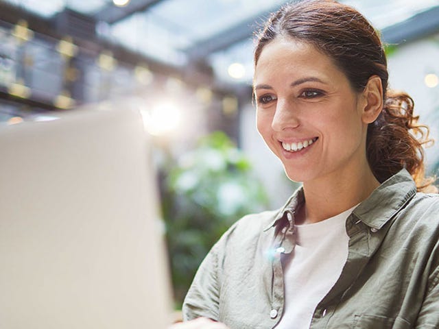 Smiling woman learning French online using a laptop in a bright, modern café.