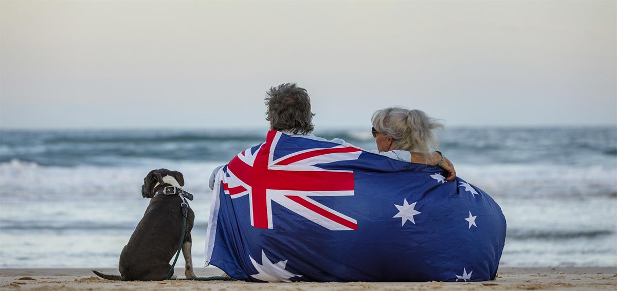 Couple with their dog holding an Australian flag on the beach.