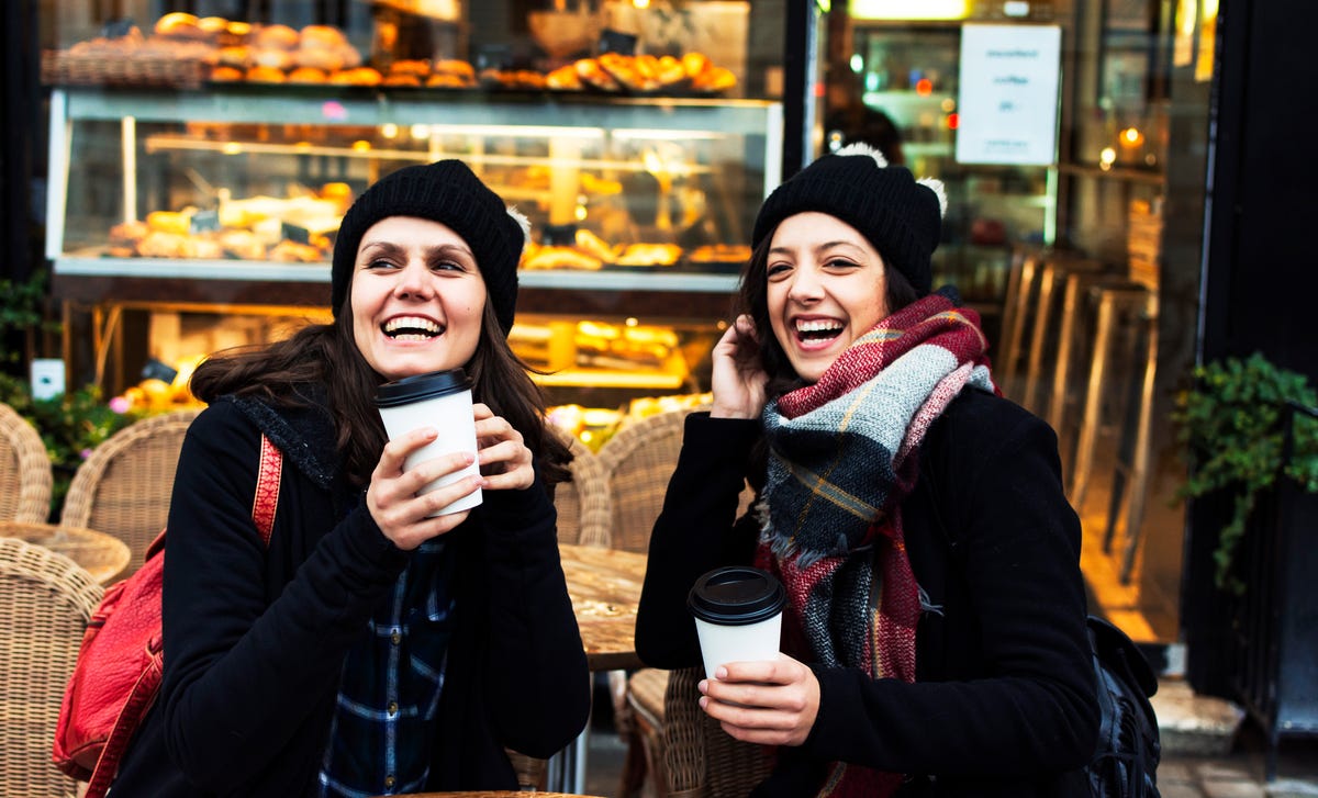 Two women enjoying coffee and laughing outside a bakery after taking Hungarian lessons together.