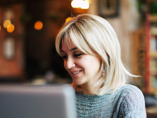 Smiling woman attending an english group class online from a cozy cafe using her laptop.