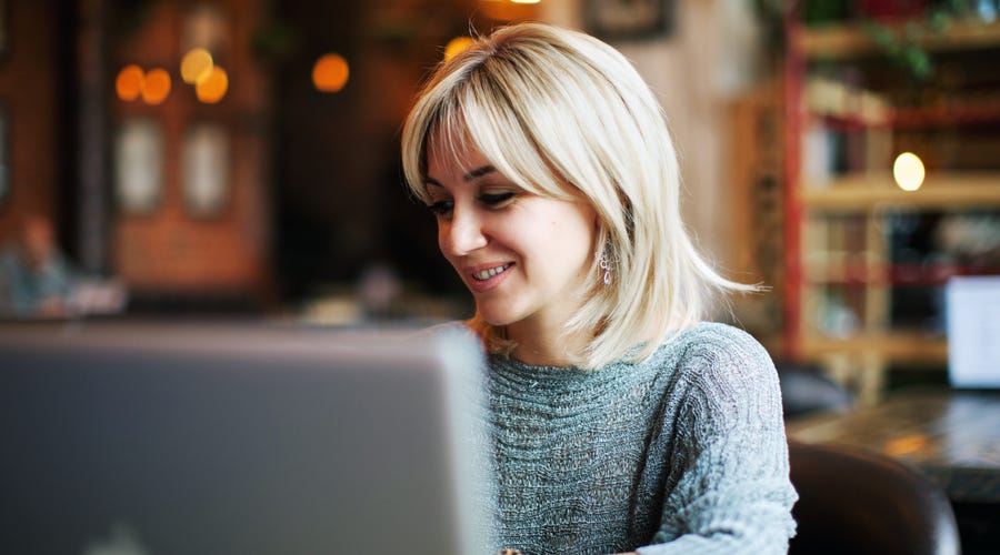 Smiling woman attending an english group class online from a cozy cafe using her laptop.