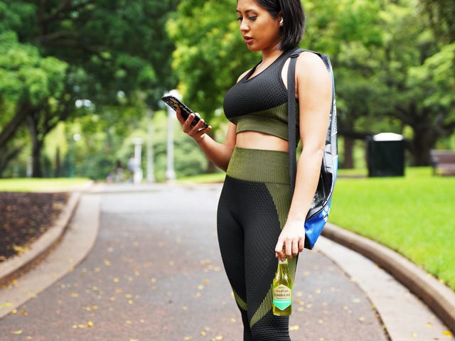 Woman in activewear looking at phone during a walk, possibly reviewing advanced English courses online