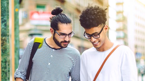 Two young men smiling while using a tablet and smartphone on a city street, representing an interactive way to learn Serbian online.