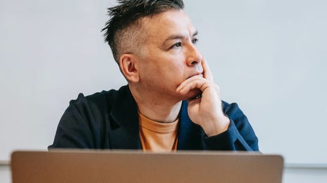 Thoughtful teacher at desk with laptop and open notebooks, considering a Dutch teaching career.