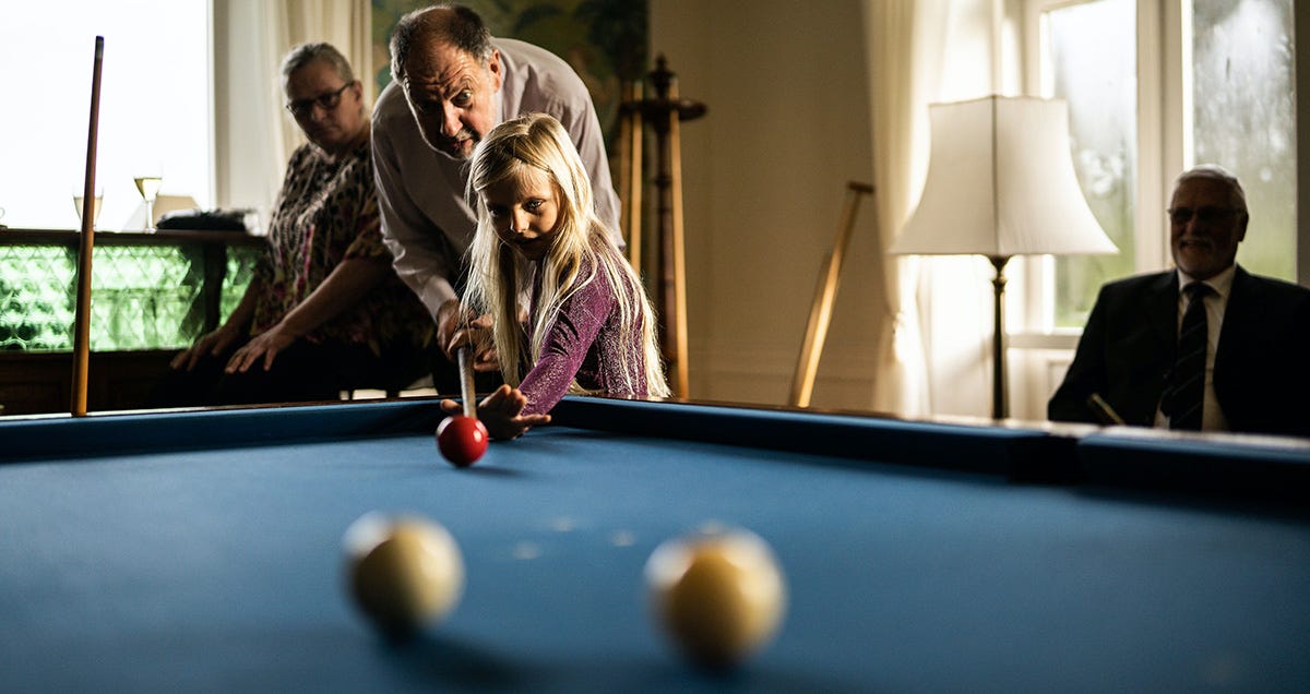 Young girl playing snooker with her grandfather in Italian.