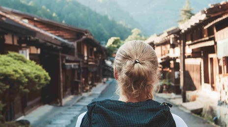 Back view of a solo traveler walking through a traditional Japanese village, symbolizing cultural immersion and language learning with Berlitz.com.