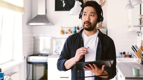 Man attending a Berlitz English course online using a tablet and headset in his kitchen workspace.