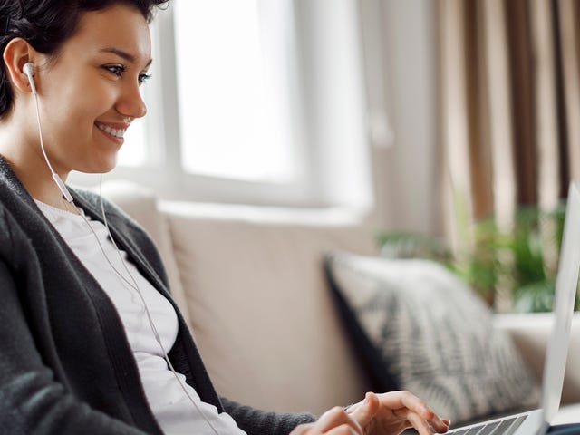 Young woman participating in an english group class online from home using a laptop and earphones.