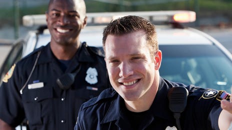 Two smiling police officers standing beside a patrol car, representing readiness for law enforcement testing and assessment