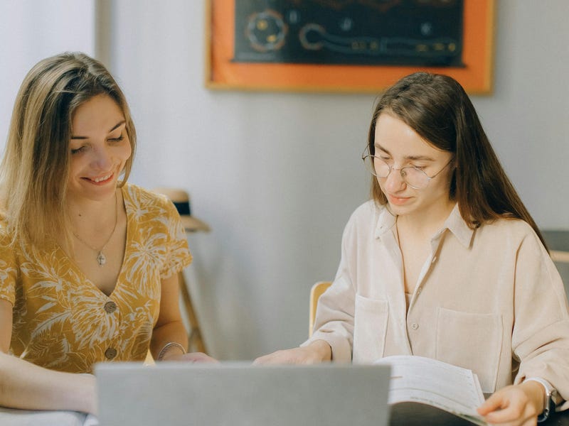 Two women studying together using books and a laptop, reflecting collaborative learning at a Berlitz language school.