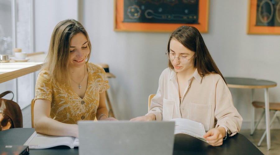 Two women studying together using books and a laptop, reflecting collaborative learning at a Berlitz language school.