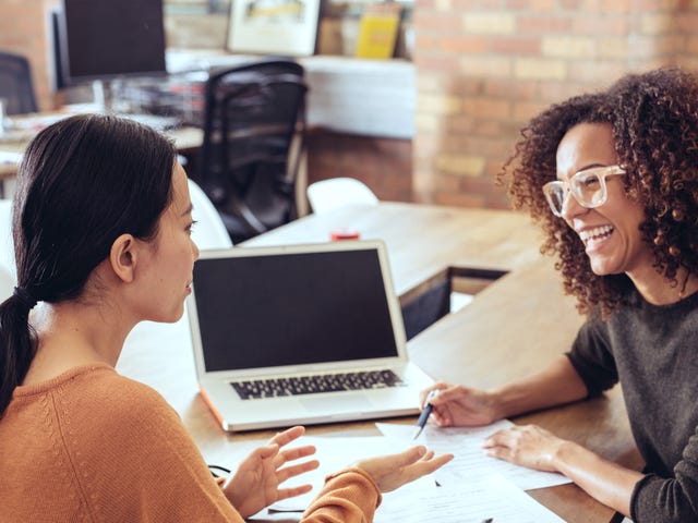 Two women in a classroom setting smiling and talking while reviewing notes during an in-person French class session