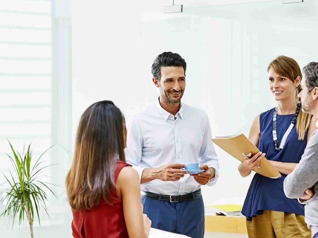 Group of multicultural professionals engaged in a conversation in a modern office, representing cultural indicators taught in Berlitz cross-cultural training programs.