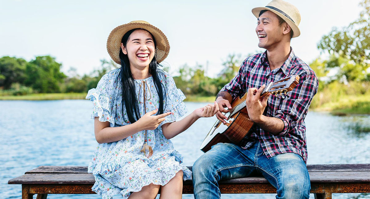 Man singing a love song to express how to say I love you in Chinese to his girlfriend, on a a bench in front of a lake.
