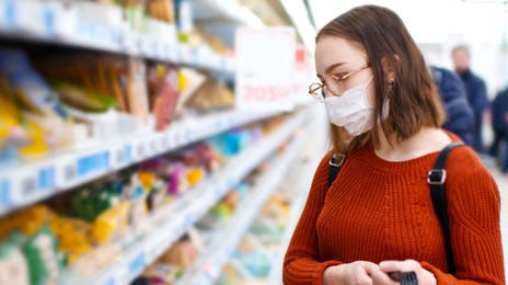 Young woman in a supermarket wearing a mask, applying language skills learned from English courses for beginners during shopping