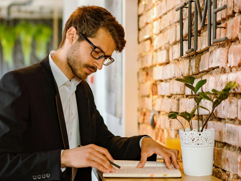 Man looking into his notebook with a pencil in his hand and practicing the present continuous tense in English