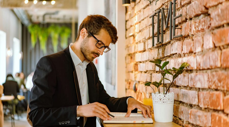 Man looking into his notebook with a pencil in his hand and practicing the present continuous tense in English