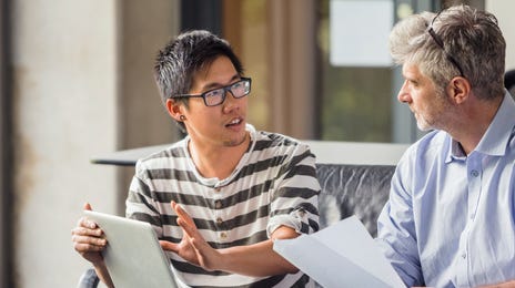 Two men engaged in a thoughtful discussion with a laptop and documents, representing mentorship and growth opportunities within Berlitz careers.