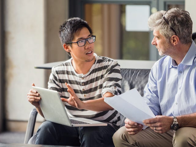 Two men engaged in a thoughtful discussion with a laptop and documents, representing mentorship and growth opportunities within Berlitz careers.