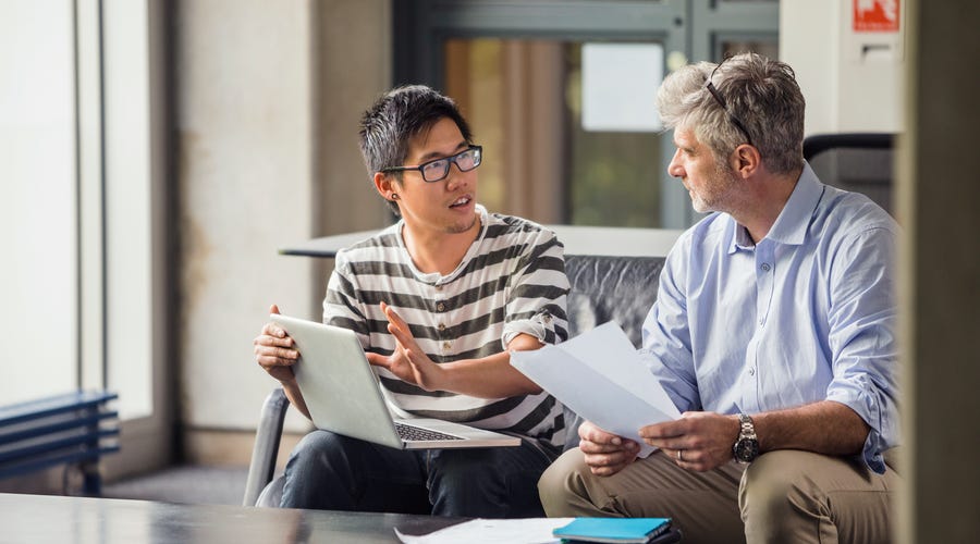 Two men engaged in a thoughtful discussion with a laptop and documents, representing mentorship and growth opportunities within Berlitz careers.