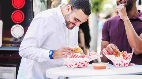 Two men enjoying a casual conversation while eating at a food truck, illustrating real-life application of Berlitz English speaking course skills.