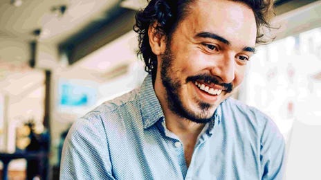 Man smiling while working on laptop in a café.